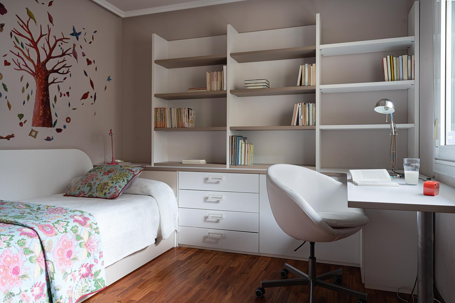 Estudio con sofá cama y librería con mesa de trabajo de color blanco