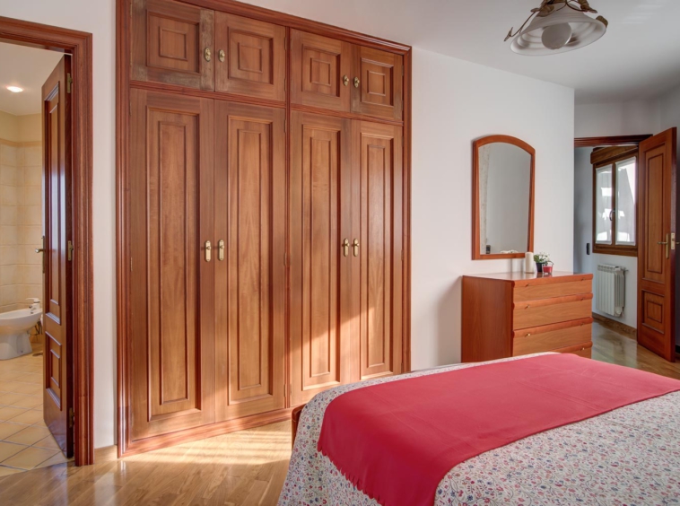 Dormitorio de matrimonio con armario empotrado de madera_ Home Staging con colcha de estampado de flores y manta coral