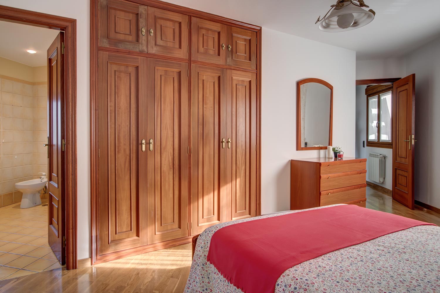 Dormitorio de matrimonio con armario empotrado de madera_ Home Staging con colcha de estampado de flores y manta coral