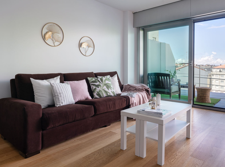 Salón+terraza bajo Costa Dulce_vistas_ Detalle del sofá marrón y la mesa blanca con decoración sencilla. Textiles claros para dar luminosidad