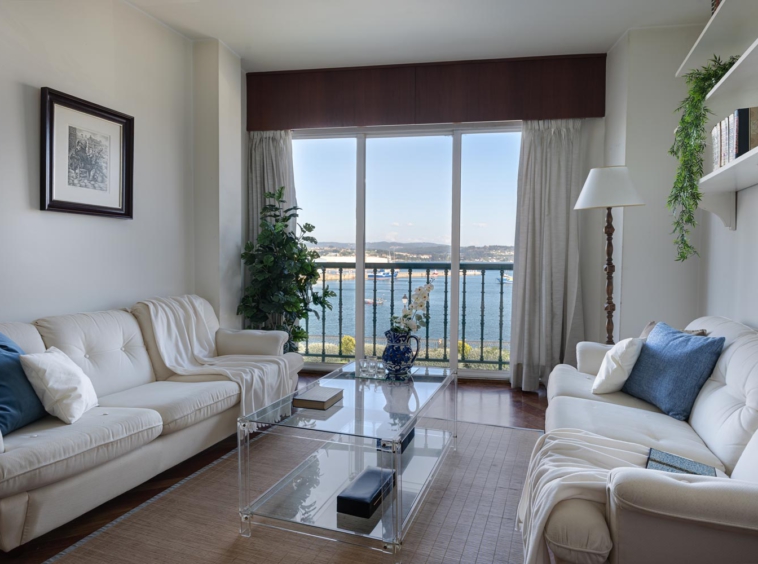 Conjunto de sofás blancos y mes de centro de metacrilato en salón con terraza y vistas al mar
