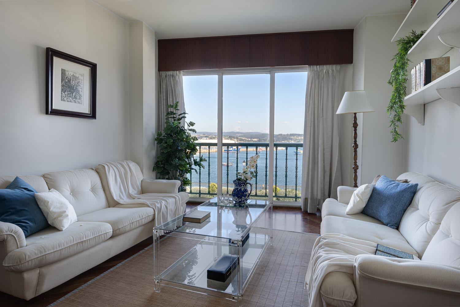 Conjunto de sofás blancos y mes de centro de metacrilato en salón con terraza y vistas al mar
