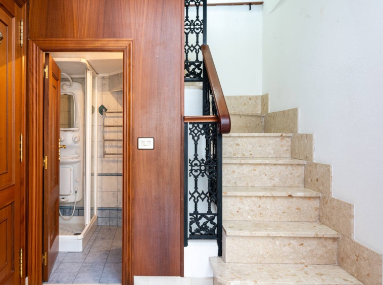 Entrada con baño bajo escaleras dúplex_ panelado de madera_forja en los pasamanos