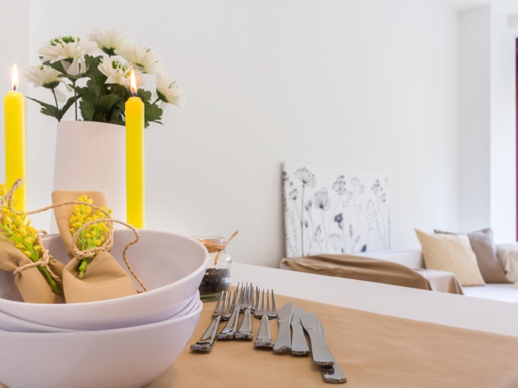 Detalle platos y cubiertos sobre mesa de comedor y velas amarillas_ Home Staging