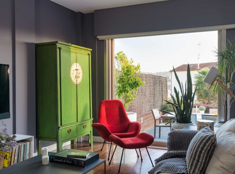 Detalle salón unifamiliar Oleiros_ sofá con textiles neutros y de rayas, butaca roja de lectura y armario de diseño verde junto a ventanal
