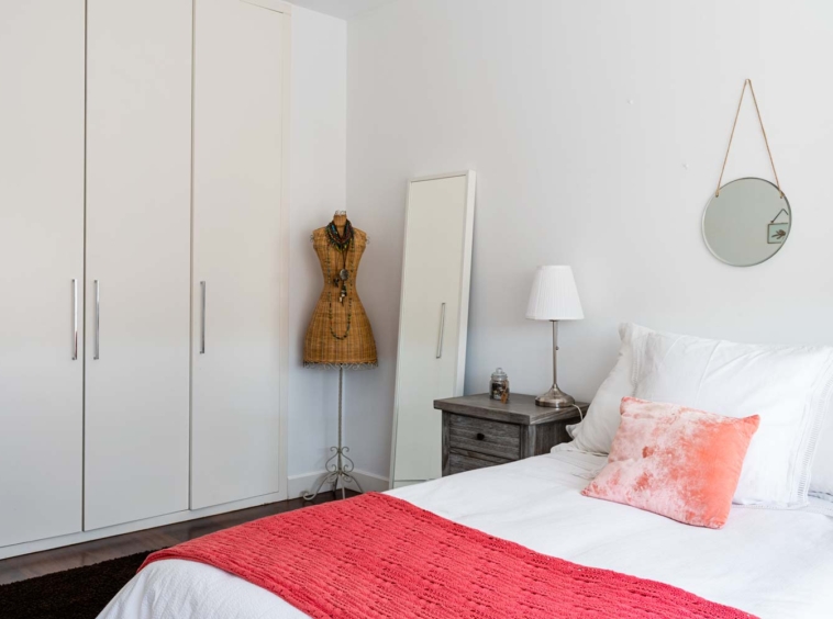 Dormitorio doble con armario empotrado y maniquí de mimbre_ Sobre la cama hay textiles en coral y blanco_ unifamiliar Oleiros