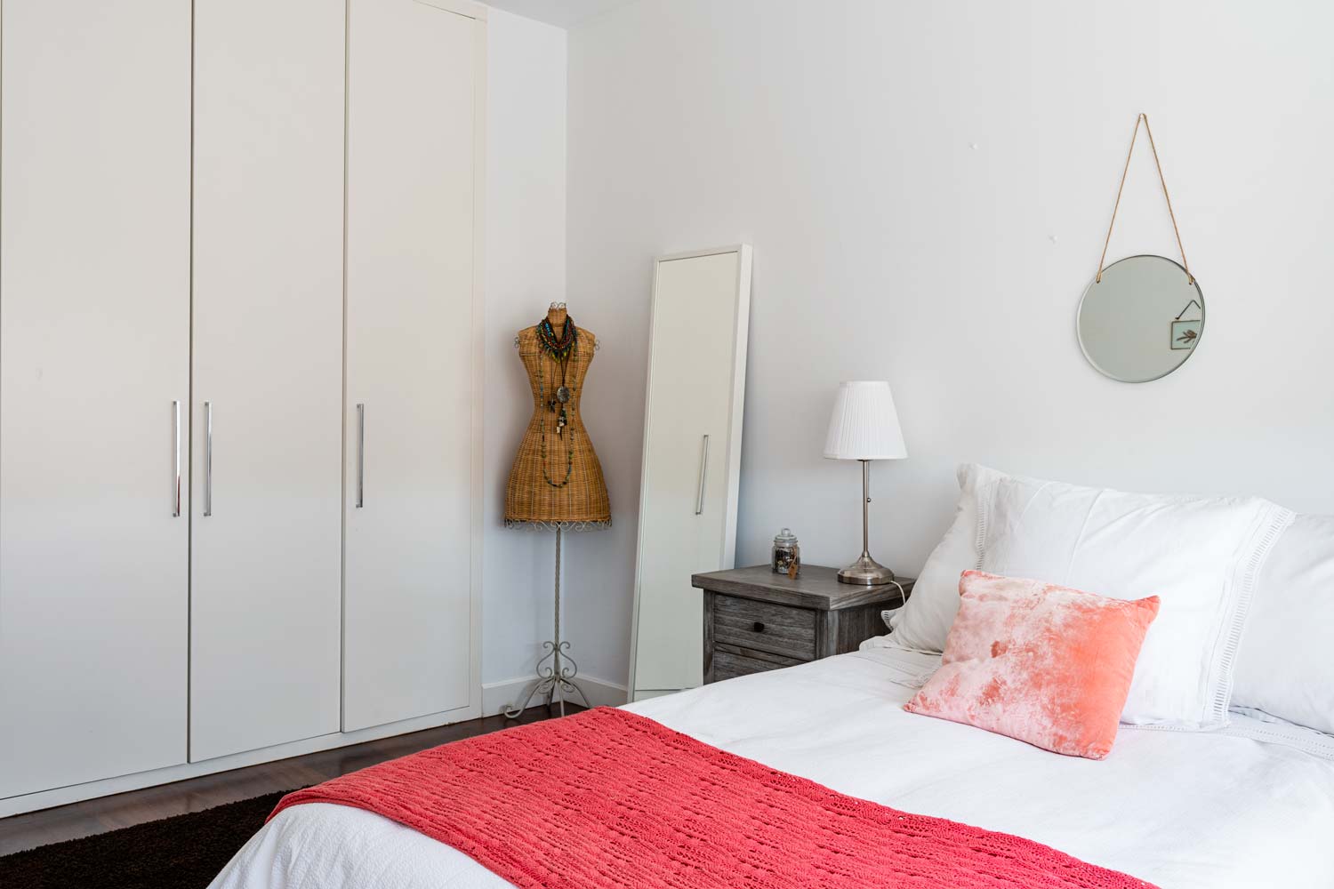 Dormitorio doble con armario empotrado y maniquí de mimbre_ Sobre la cama hay textiles en coral y blanco_ unifamiliar Oleiros