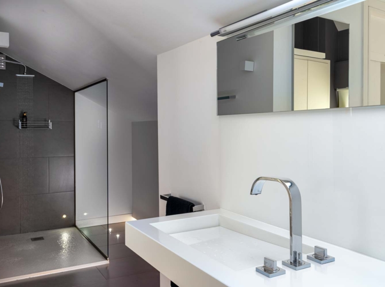 Cuarto de baño planta alta vivienda unifamiliar Oleiros_ En primer plano lavabo con grifería de diseño y al fondo ducha con mampara