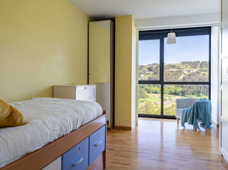 Dormitorio individual amarillo con gran ventanal y butaca junto a él_vistas a la naturaleza