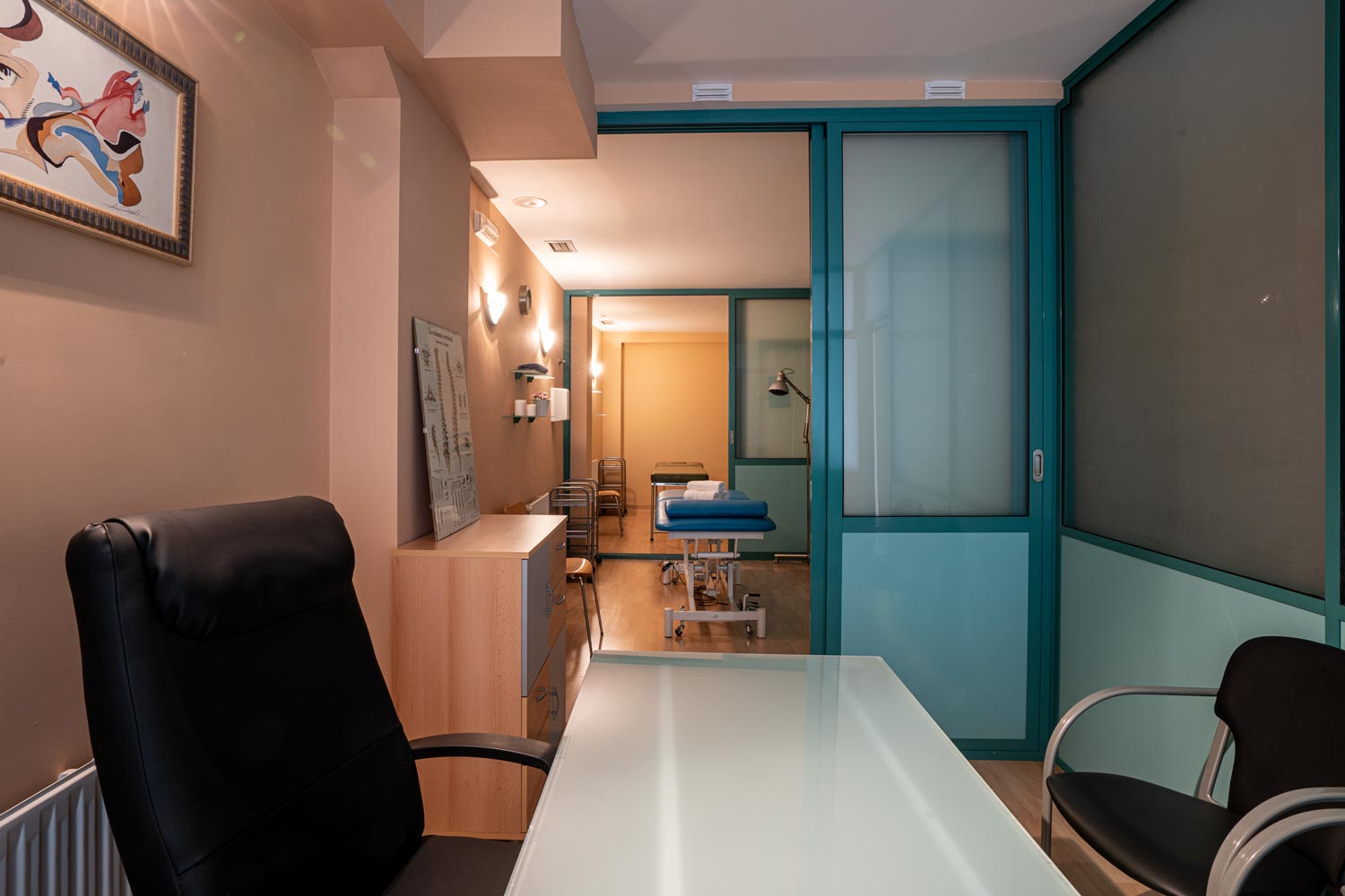 Interior de local comercial terapias naturales. Vemos el despacho y distintos gabinetes con camillas azules comunicados por puertas verdes abiertas