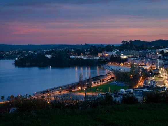 Finca en venta en Sada, A Coruña con vistas al atardecer sobre el mar, destacando la iluminación urbana y costera.