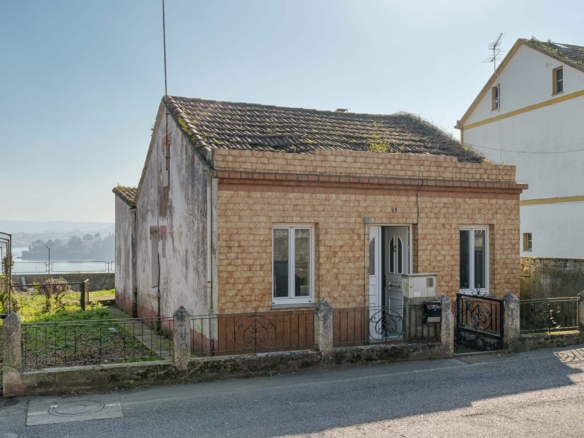 Fachada de una pequeña casa con tejado a dos aguas y vegetación creciendo, ubicada en una tranquila calle de Sada y vistas al mar