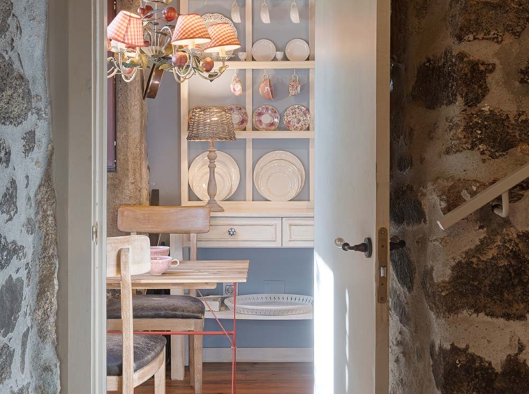 Vista de una acogedora cocina rústica desde la puerta, con una mesa pequeña y estantes con platos decorativos.