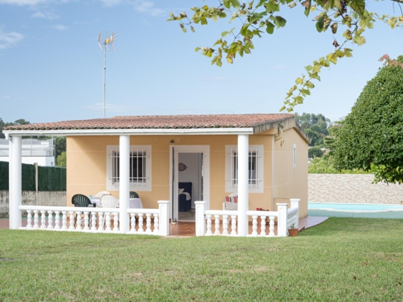 Vista exterior de una casa de una planta con fachada en tonos amarillos, porche con columnas blancas y jardín bien cuidado. La propiedad está en venta por Morando Inmobiliaria en Sada.