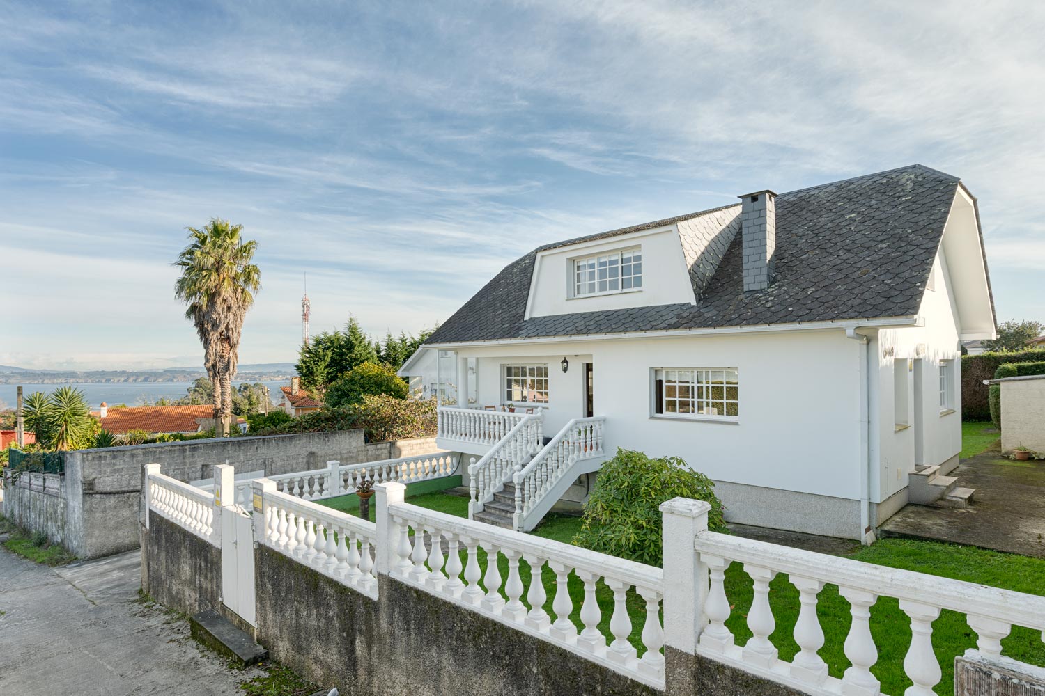 Casa en venta en Sada por inmobiliaria Morando, con amplio jardín, fachada blanca, tejado de pizarra y vistas al mar.