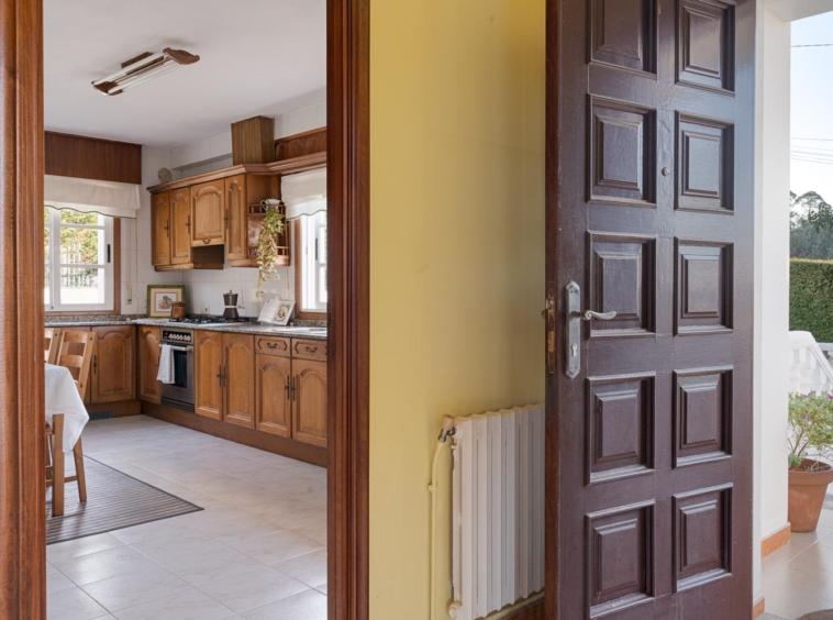 Entrada principal con puerta de madera y vista a la cocina rústica de madera en casa en venta en Sada.