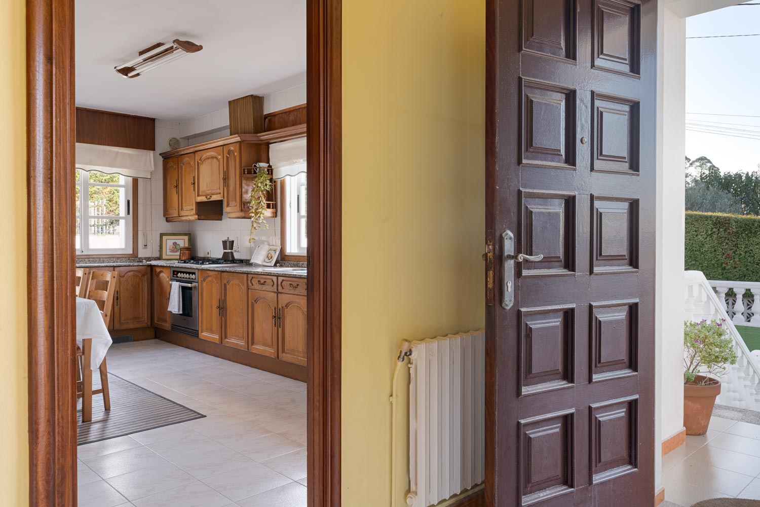 Entrada principal con puerta de madera y vista a la cocina rústica de madera en casa en venta en Sada.