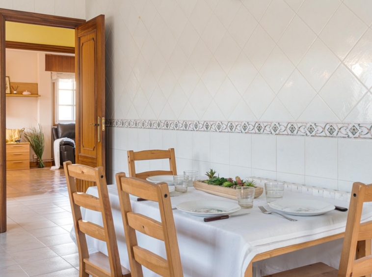 Cocina acogedora con mesa preparada y sillas de madera en una cocina con paredes de azulejos en casa en venta en Sada.