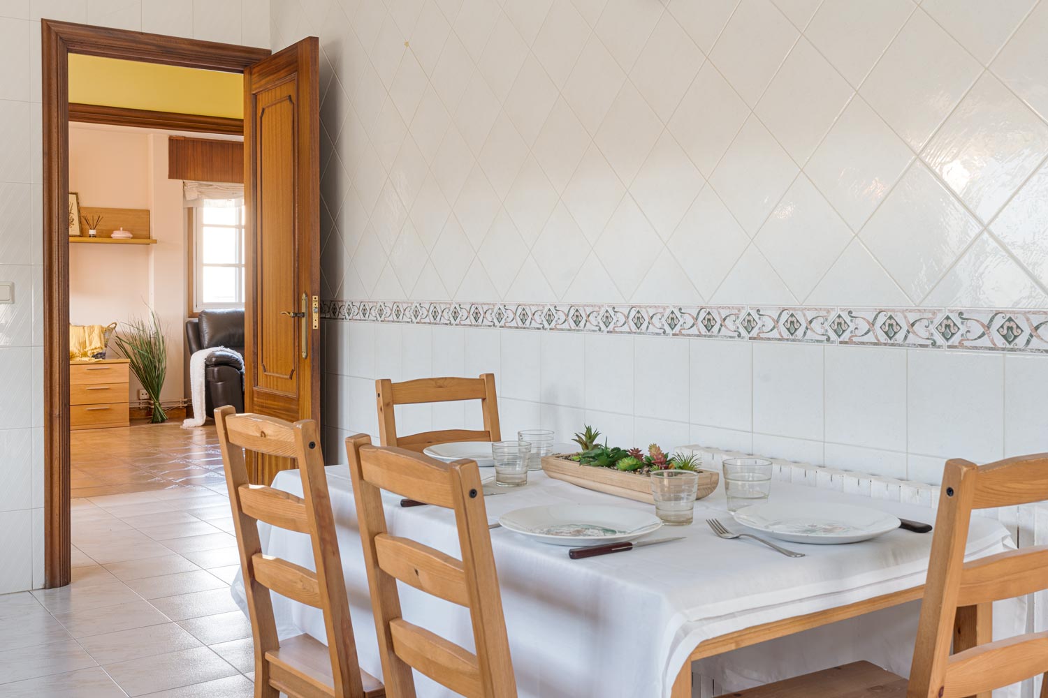 Cocina acogedora con mesa preparada y sillas de madera en una cocina con paredes de azulejos en casa en venta en Sada.