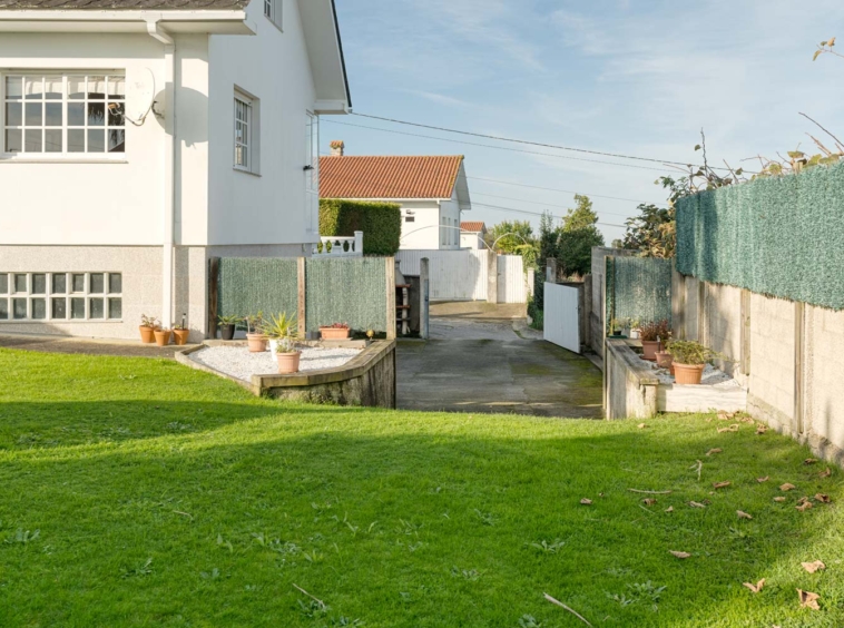 Casa en venta en Sada con jardín lateral cuidado, césped verde y plantas decorativas.