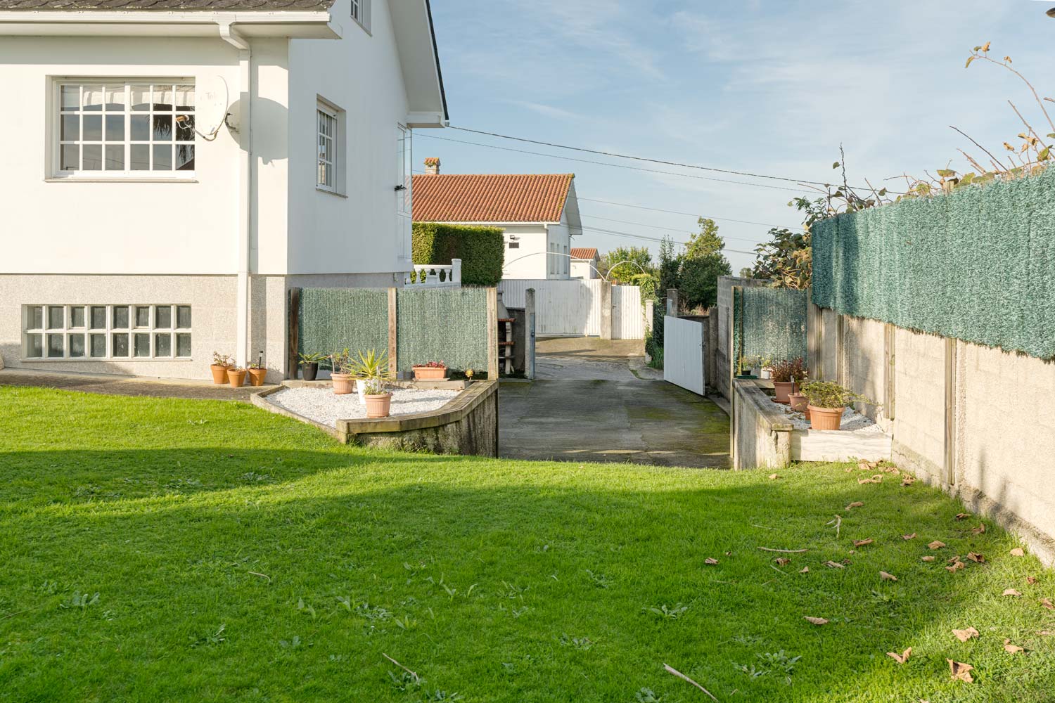 Casa en venta en Sada con jardín lateral cuidado, césped verde y plantas decorativas.