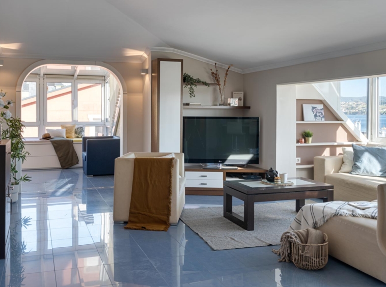 Salón espacioso con sofá beige, televisor y vistas al puerto en piso en venta en Sada por inmobiliaria Morando.